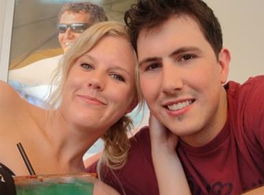 Close-up of smiling young couple enjoying drinks at a casual outdoor gathering.