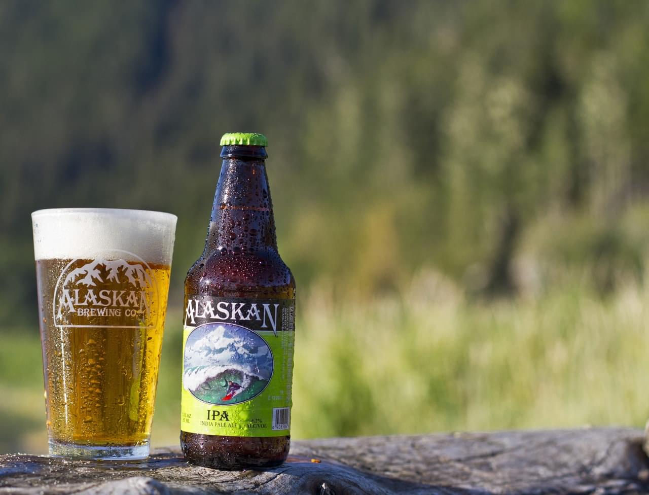 Alaskan IPA beer bottle with a frosty glass of cold beer placed outdoors on a rustic wooden surface.