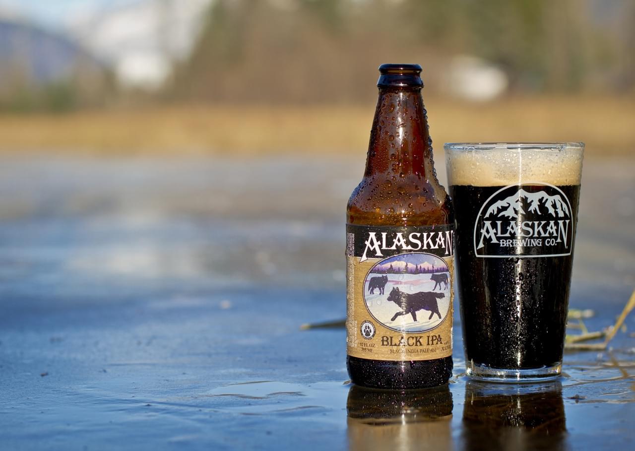 Alaskan Black IPA craft beer bottle and glass outdoors, showcasing rich dark ale from Alaska Brewing Co.