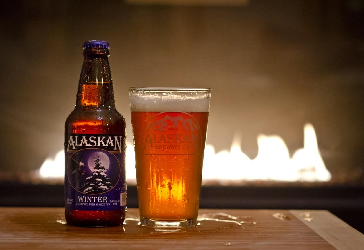 Close-up of Alaskan Winter Ale bottle and filled glass with a cozy fire in the background.