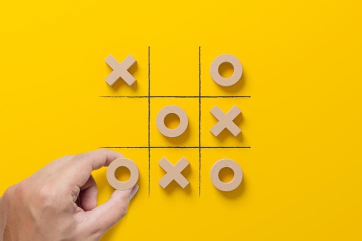 Close-up of hand playing tic tac toe game on yellow background, wooden game pieces, and grid.